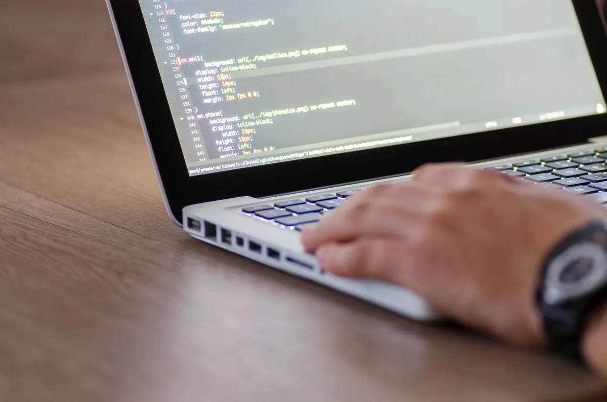 Hands typing website code on a laptop